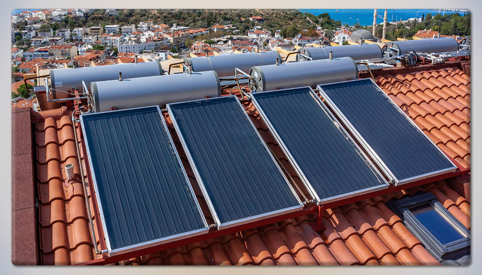 Four flat-plate solar thermal collectors and storage tanks installed on a tiled roof for residential hot water.